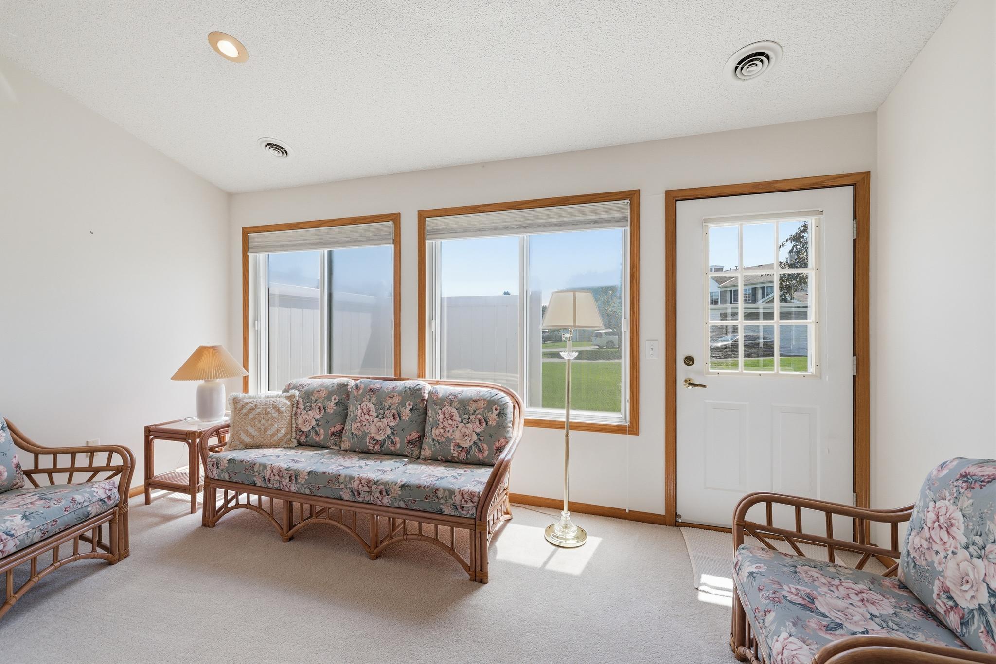 Bright, glass-lined sunroom filled with natural light, featuring comfortable seating and a clear view through the doorway to the inviting patio just outside.