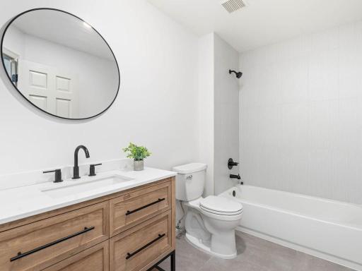 Upper-level full bath features wood-tone vanity, black fixtures, tile flooring, and tub/shower combination w/tiled surround.