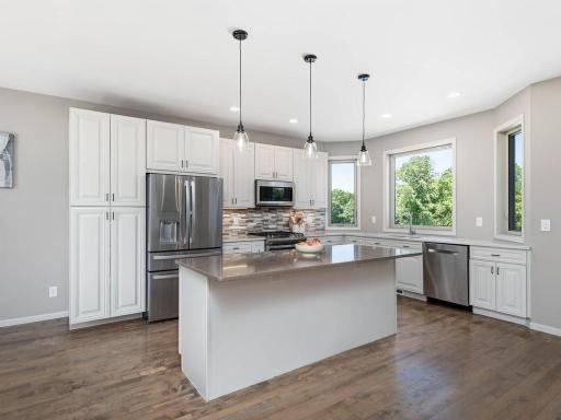 Bright main level kitchen features quartz countertops, SS appliances, abundant cabinetry, and Lg ctr island w/seating while multiple windows bring in natural light and views of the surrounding acreage.