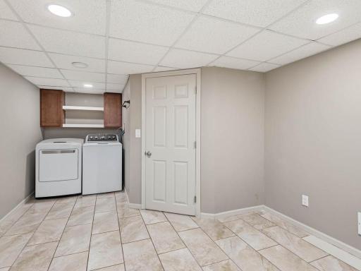 Second laundry room in LL includes gas dryer hookup, cabinetry, open shelving, tile flooring, and additional storage.