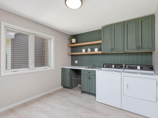 Stylish main level laundry room features electric dryer hookup, utility sink, cabinetry, open shelving, and tile flooring for added everyday convenience.