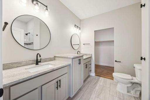 Main level primary bathroom with two sinks, tile flooring and large walk-in closet - *Photo of previous spec - colors may vary on current spec home*