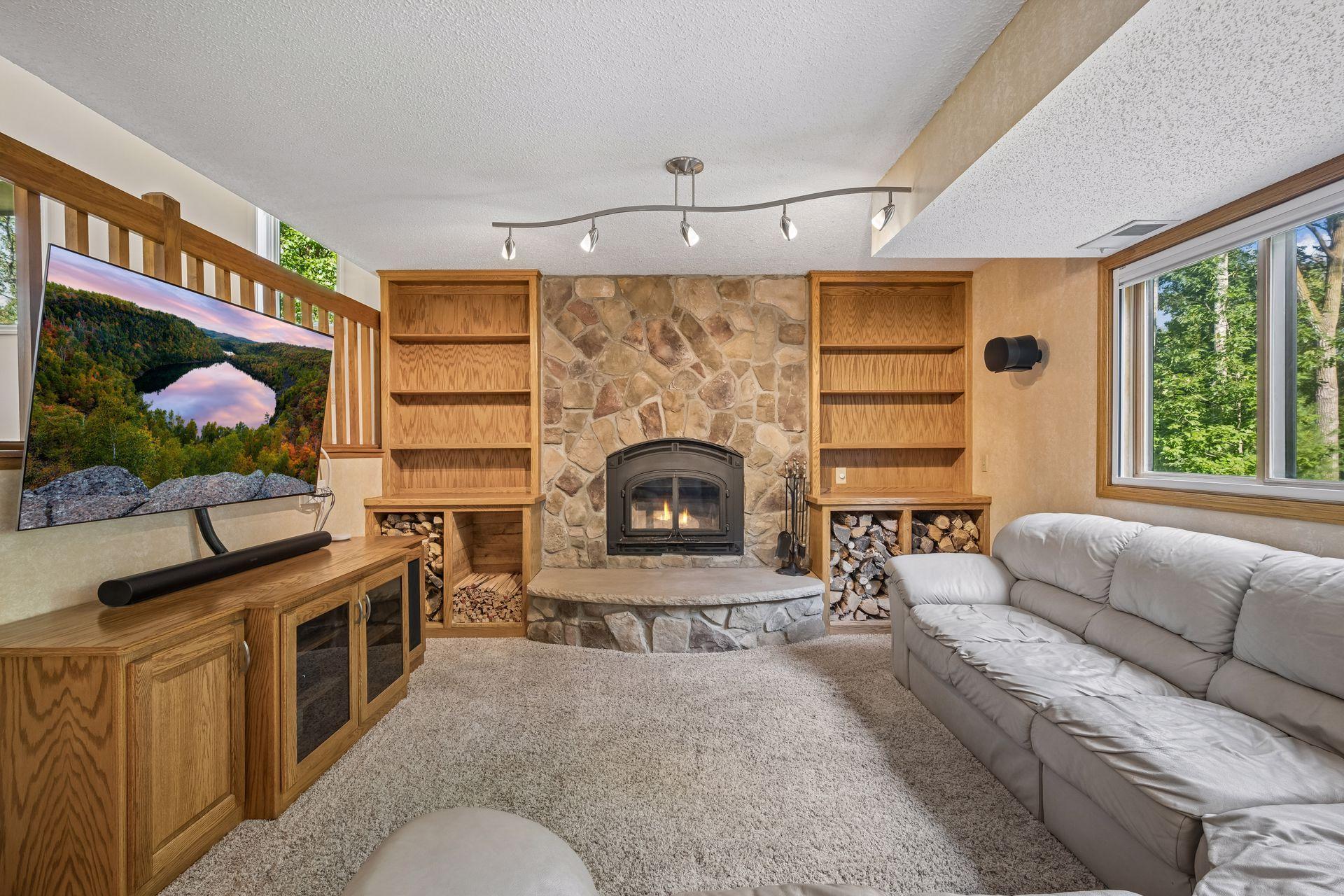 Built-in cabinetry surrounding the hearth offer convenient storage for firewood. Black-out shades can cover the window for cozy movie nights in. Matching oak and glass media console will remain with the home.