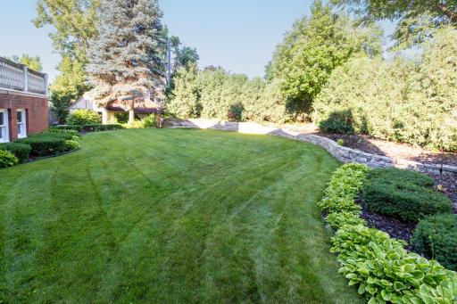 Beautifully landscaped grounds feature a curved lawn, stone retaining walls, and mature privacy trees