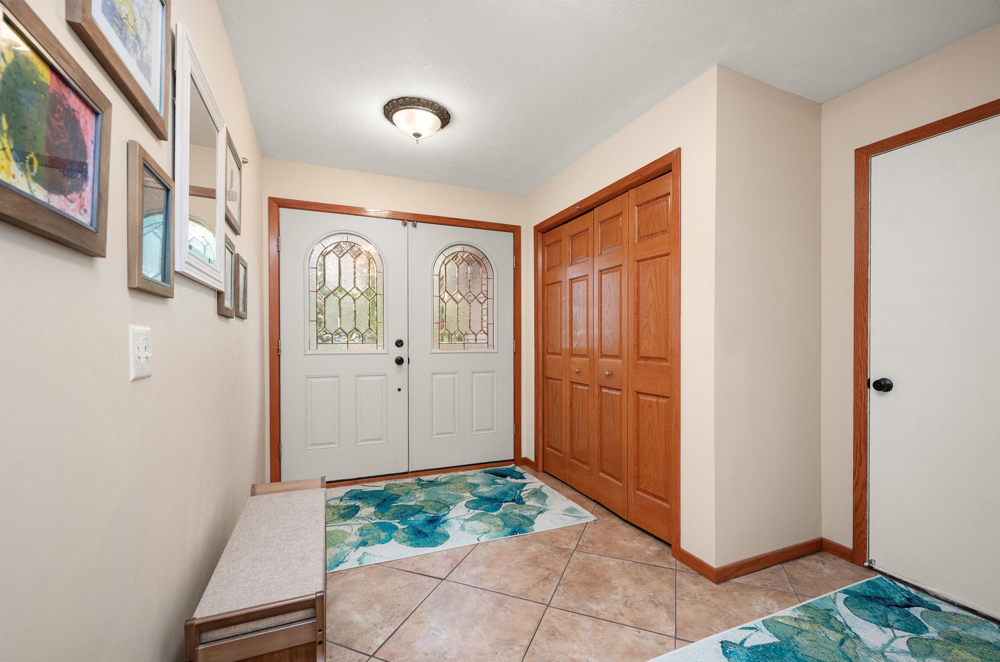 Grand entryway with double front doors, tiled flooring, built-in bench seating, and expansive closet storage