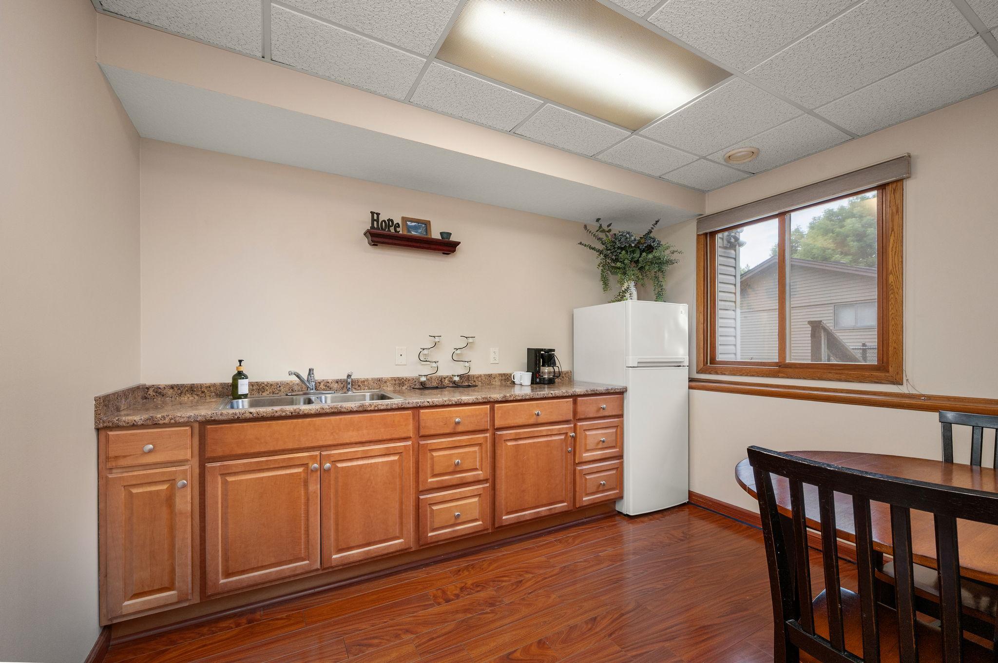 Convenient lower-level kitchenette area equipped with oak cabinetry, sink, and full-size refrigerator space