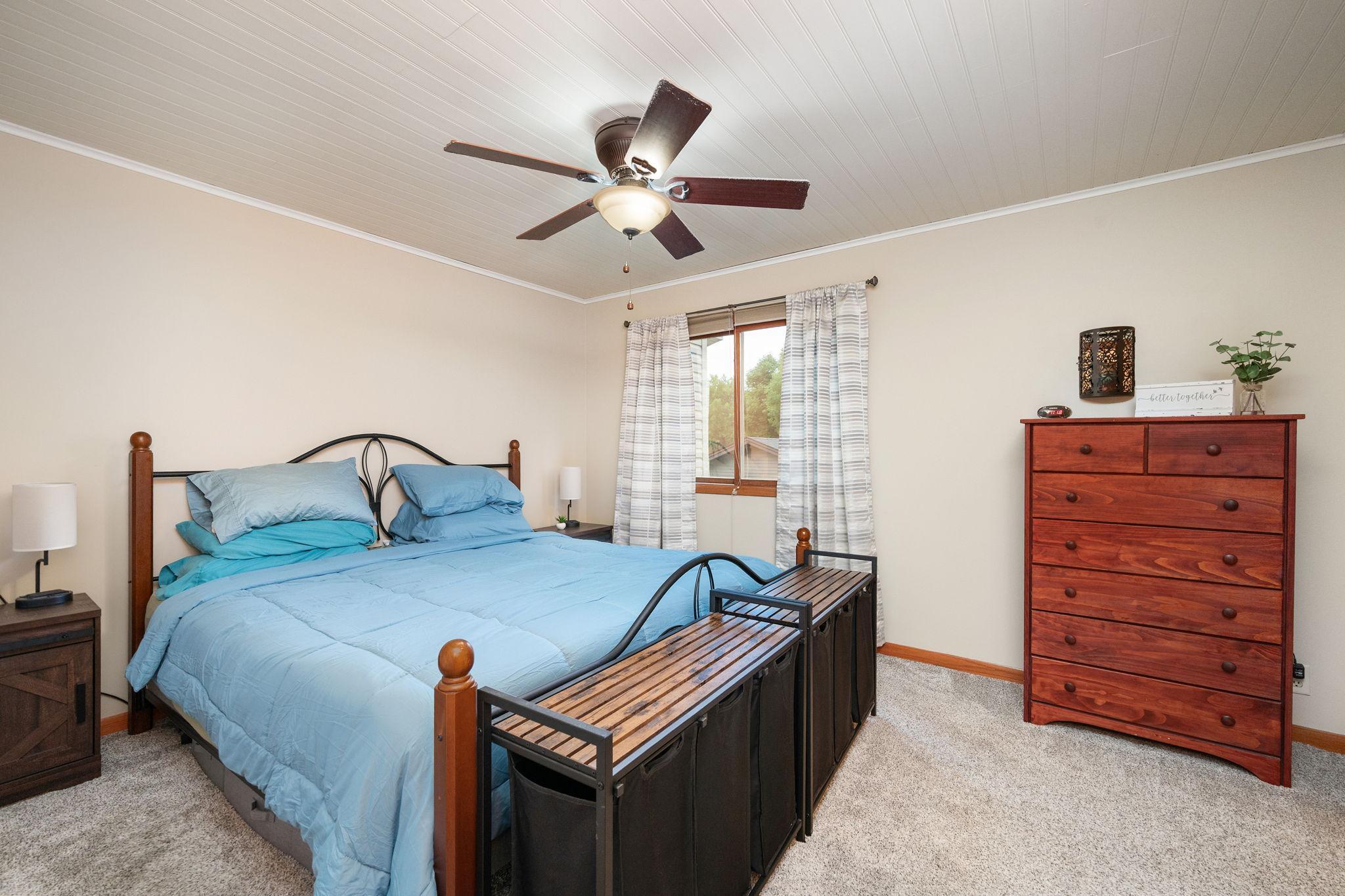 Generous primary bedroom with a cooling ceiling fan, warm wood trim accents, and ample natural light