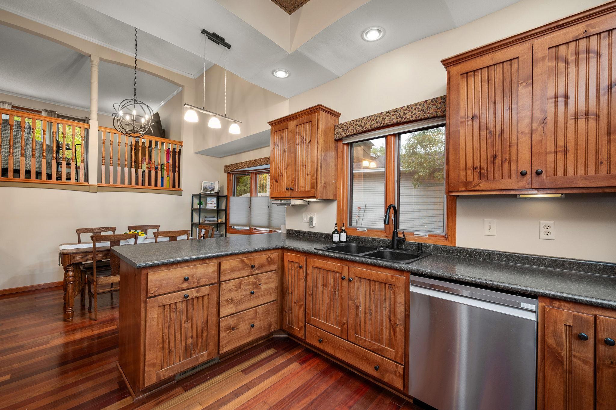 Alternate view of the kitchen showcasing rich cabinetry, recessed lighting, hardwood floors, and a large window above the sink