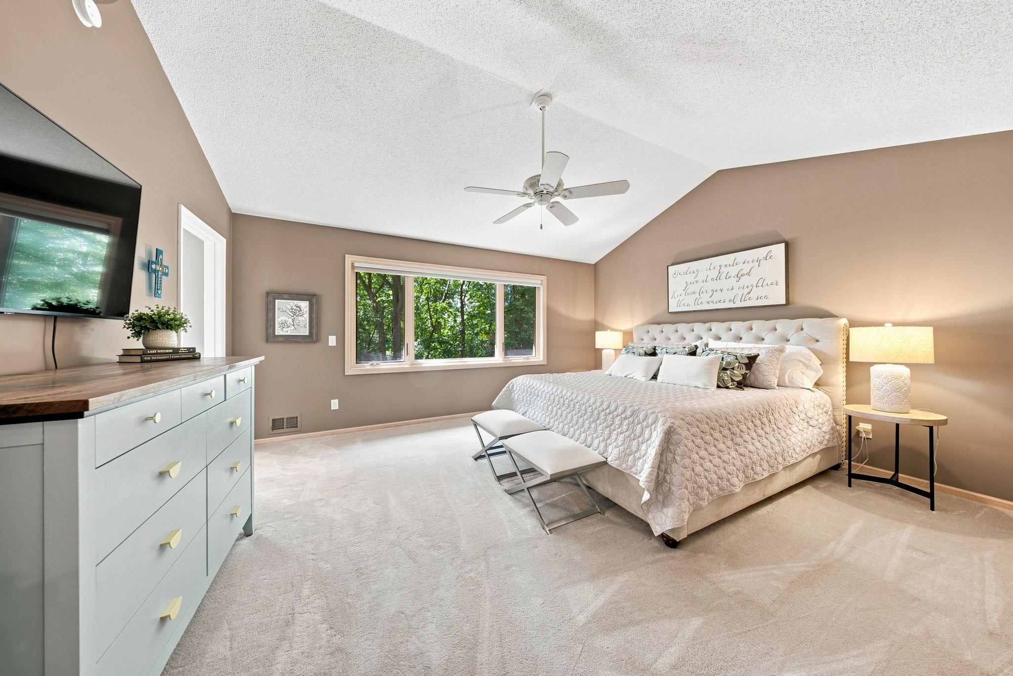 The vaulted primary bedroom overlooks the lush backyard