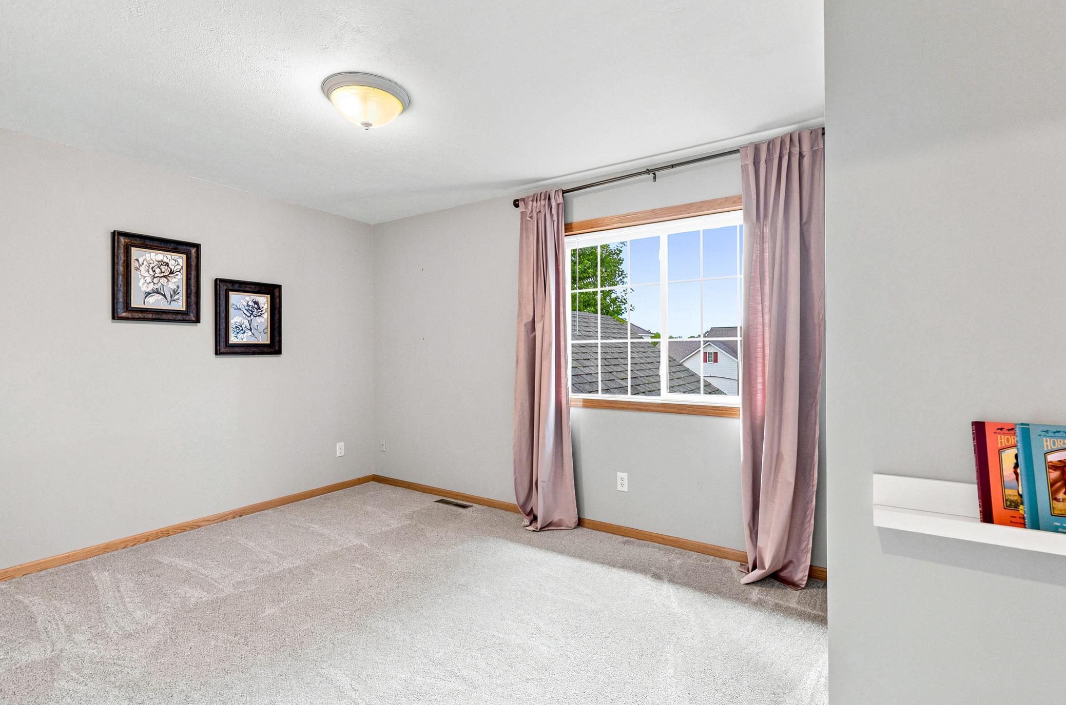 Spacious second bedroom upstairs featuring a large window, plush carpeting, and ample space for family, guests, or a home office.
