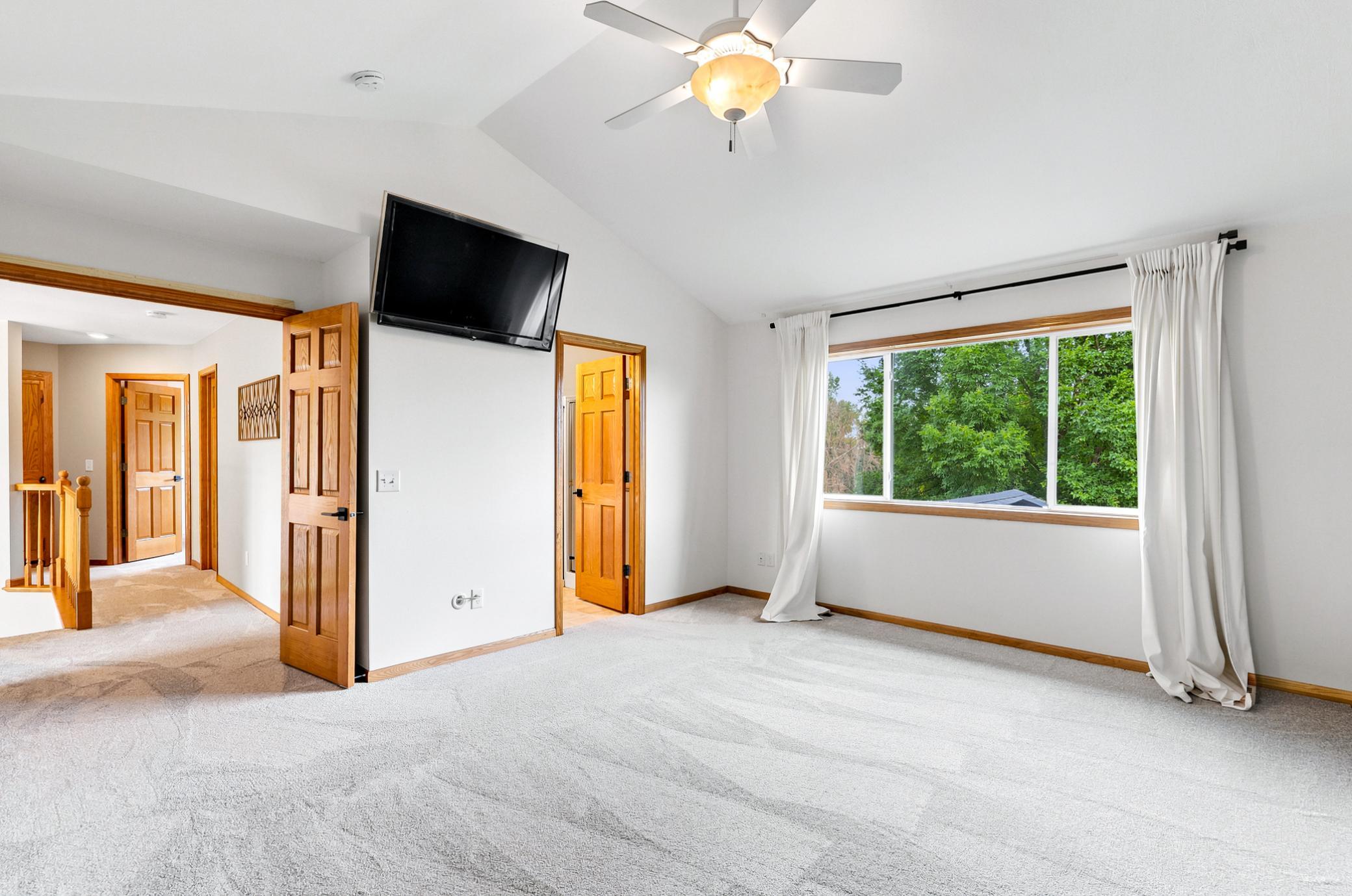 The expansive primary bedroom offers room for a king-sized suite, a vaulted ceiling with ceiling fan, and a peaceful atmosphere designed for relaxation.