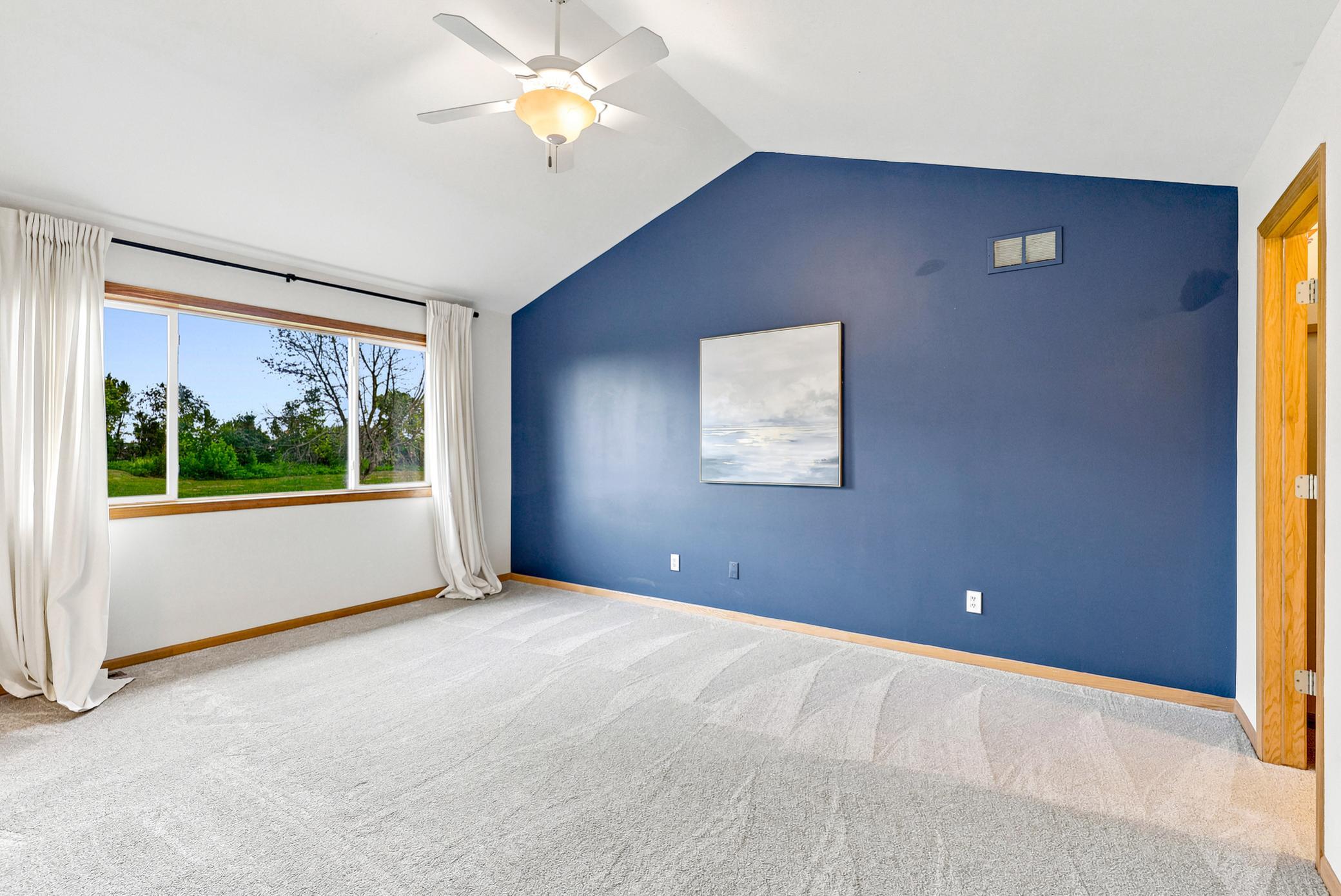 Retreat to the spacious primary suite featuring a vaulted ceiling, designer accent wall, abundant natural light, and serene views overlooking the Boulder Pointe Golf Course.