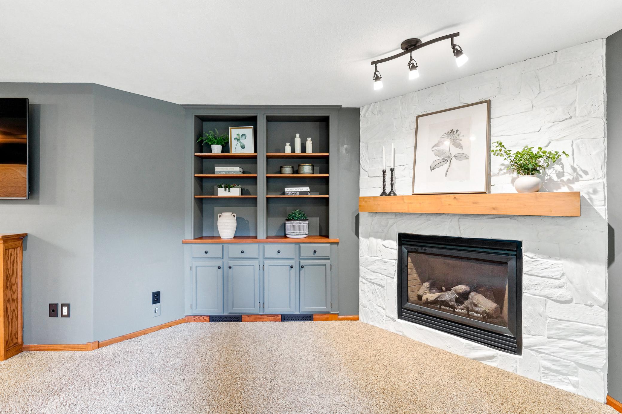 Custom built-in cabinetry and display shelving frame a stunning stone gas fireplace with rustic wood mantel, creating a warm and inviting focal point for the recreation room.