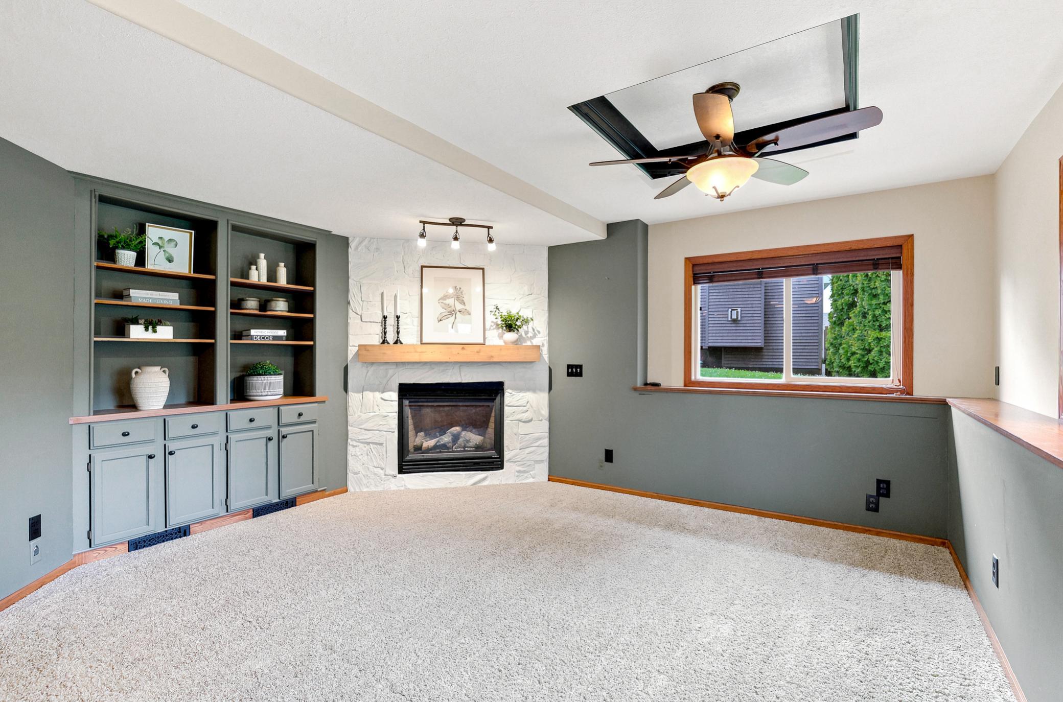 An exceptional recreation room designed for gathering, complete with custom built-in cabinetry, striking stone gas fireplace with rustic wood mantel, tray ceiling detail, and ample space for movie nights, game day, or everyday relaxation.