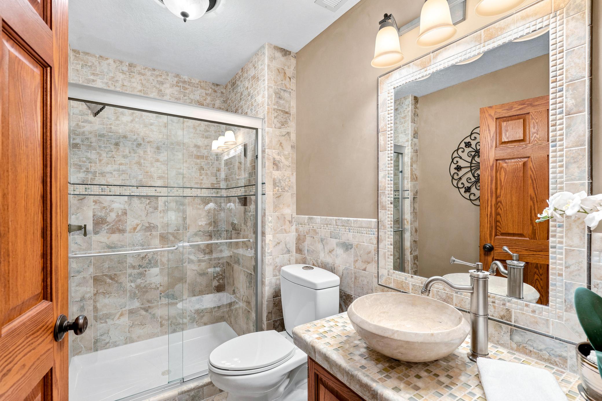 Beautifully updated lower-level ¾ bath featuring a custom tiled walk-in shower with glass doors, vessel sink vanity, and upscale finishes that add a touch of luxury.