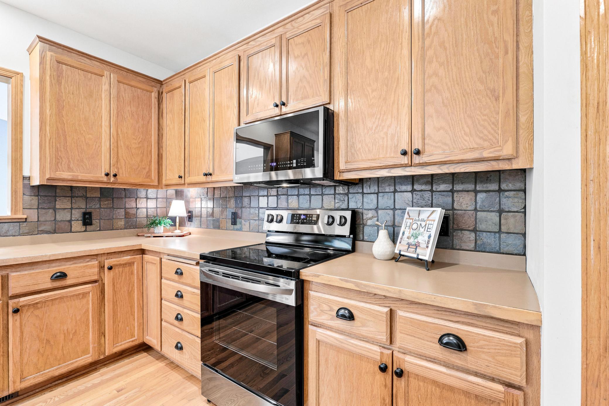 The chef's kitchen offers abundant oak cabinetry, generous countertop workspace, stainless steel appliances, and a timeless tile backsplash designed for both function and style.