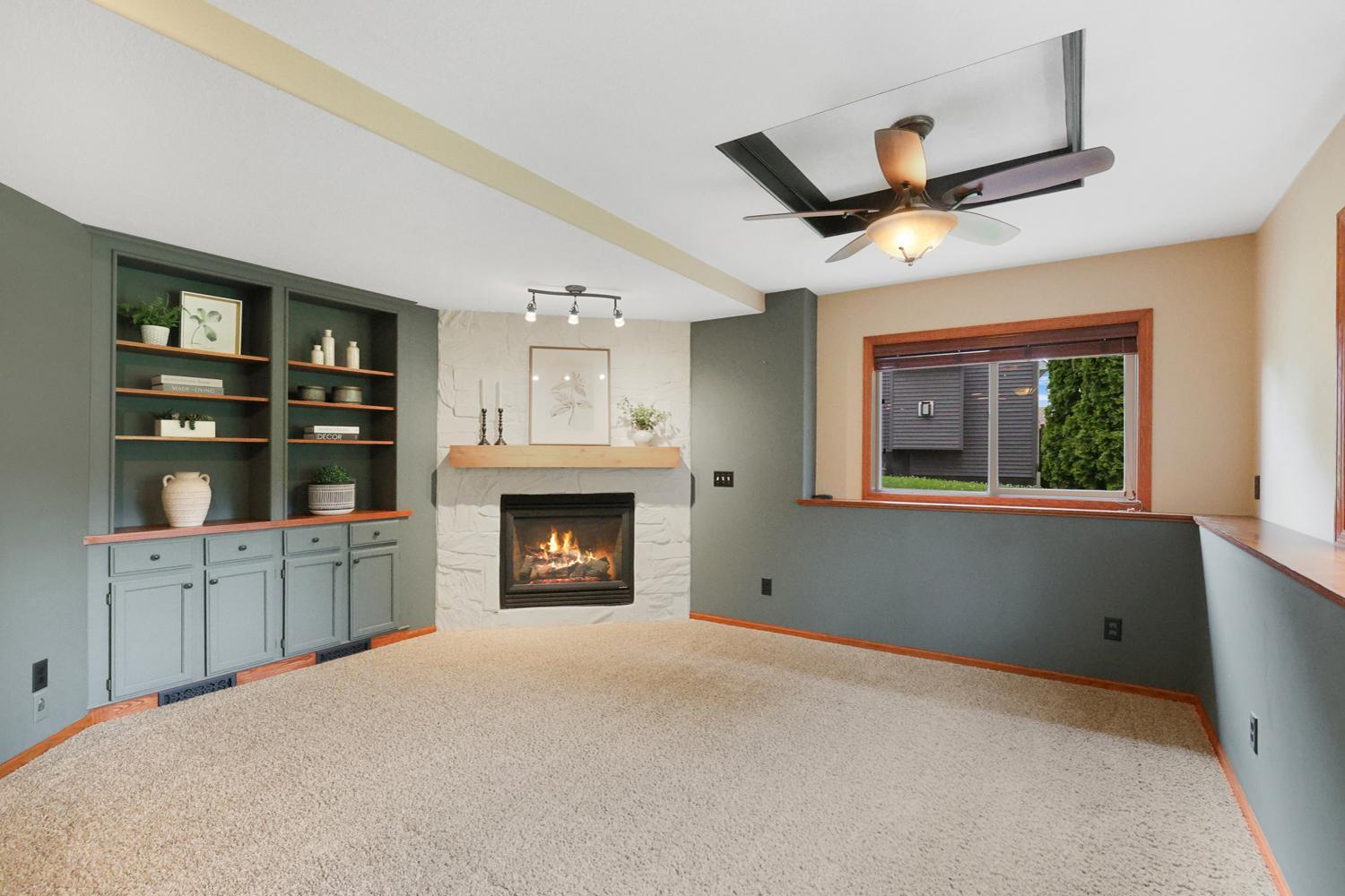 An exceptional recreation room designed for gathering, complete with custom built-in cabinetry, striking stone gas fireplace with rustic wood mantel, tray ceiling detail, and ample space for movie nights, game day, or everyday relaxation.