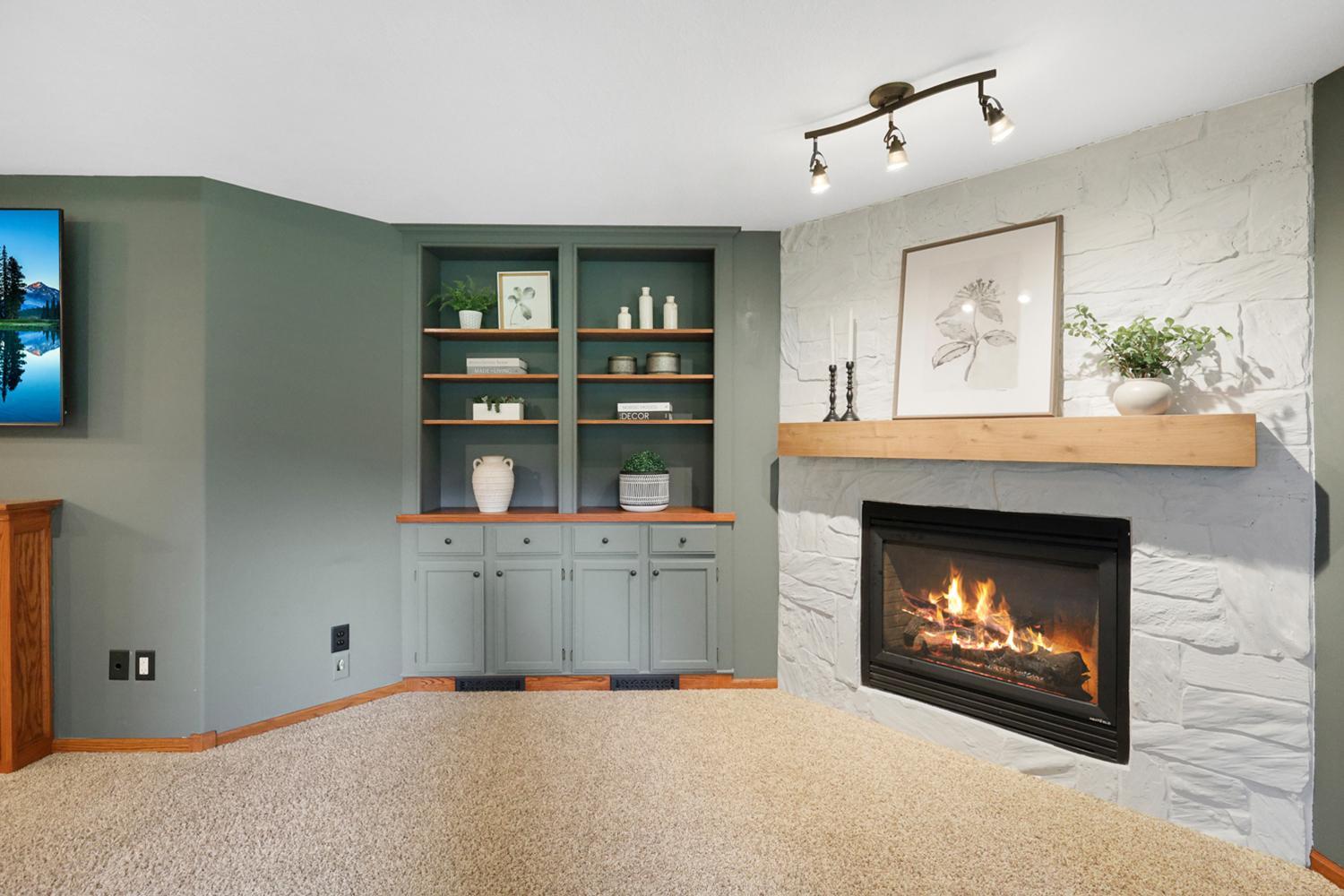 Custom built-in cabinetry and display shelving frame a stunning stone gas fireplace with rustic wood mantel, creating a warm and inviting focal point for the recreation room.