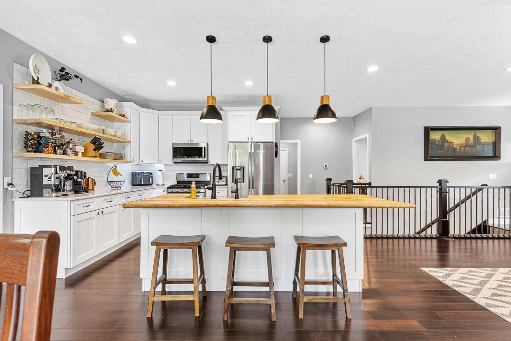 This kitchen is a chef's delight - large center island with a custom wood countertop and farm house sink, decorative matching floating shelves, and stainless steel appliances