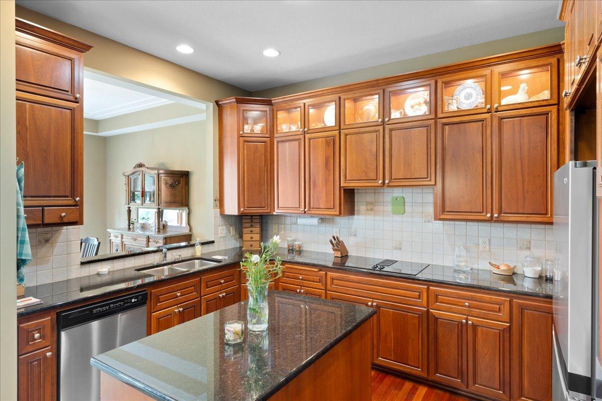The beautifully appointed kitchen features custom cherry cabinetry with illuminated display cabinets, granite countertops, and stainless steel appliances, creating an elegant and functional space that is ideal for both everyday living & entertaining.