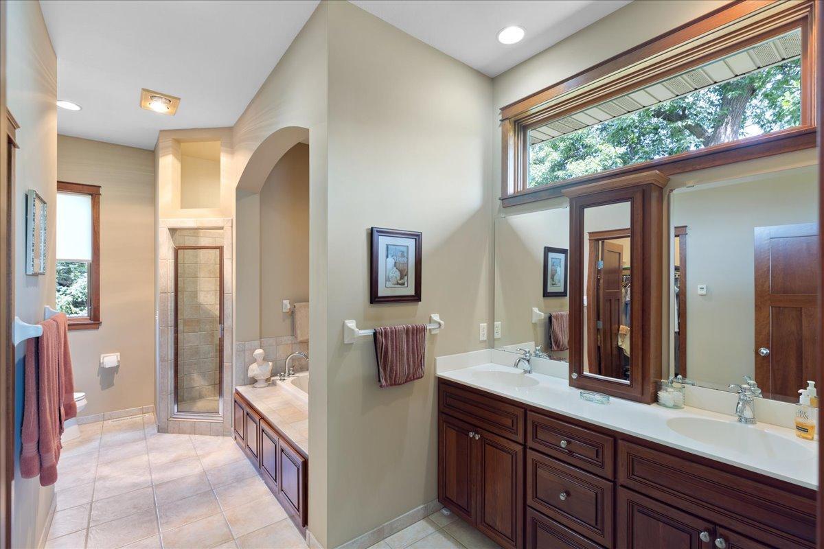 The luxurious primary bath is designed to spoil you, featuring heated tile floors, dual vanities with custom cabinetry, and an upper transom window that fills the space with natural light.