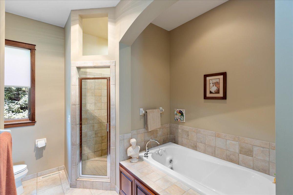Wrapped in beautiful ceramic tile, the primary bath features a large jetted soaking tub nestled within an elegant arched alcove, complemented by a separate walk-in shower for a truly relaxing, spa-like experience.