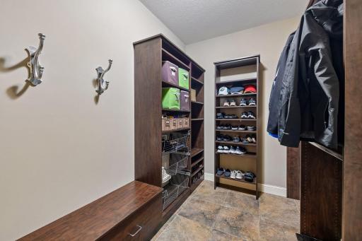 A functional mudroom featuring ceramic tile floors, a built-in bench, open shelving, wire baskets, and hanging space for added convenience. The mudroom leads to the attached 1000+sf garage that is heated, fully finished and wired for an EV charger.