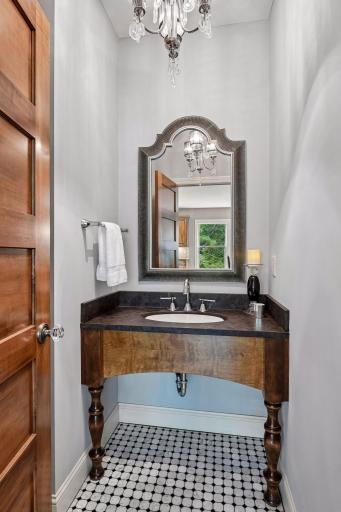 A beautifully detailed powder room featuring a dresser-inspired vanity, mosaic tile floor, ornate mirror, and chandelier.