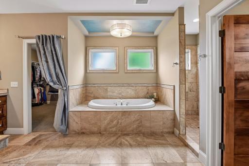 A spacious primary bath with a 6-foot jetted tub, privacy-glass windows, and elegant tray ceiling detail. The doorway to the left leads to the 11x10 walk-in closet.