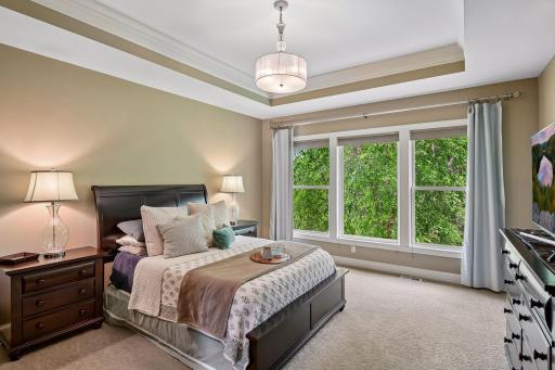 The primary bedroom features a large, detailed tray ceiling with crown molding in the inset and a stylish drum chandelier.