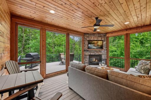 A cozy screened porch with a gas fireplace, wood plank ceiling, fan, and recessed lighting, plus maintenance-free decking that extends seamlessly to the attached deck.