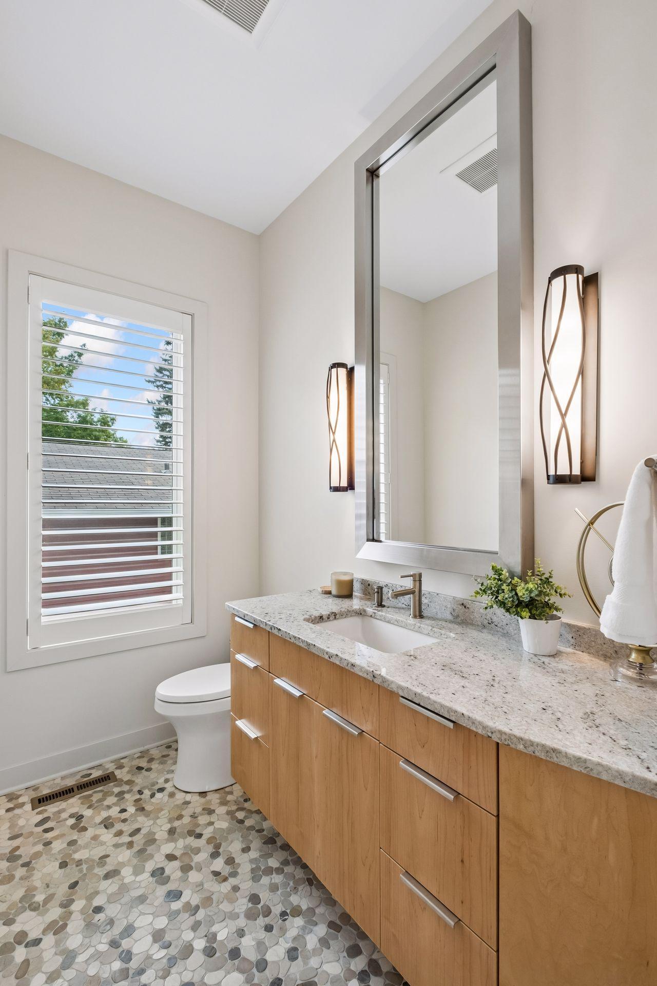 Main level half bath with pebble stone heating flooring to feel like you're at the beach. Beautiful granite vanity and lighting accent this powder bath located off the kitchen and hallway from main entrance.