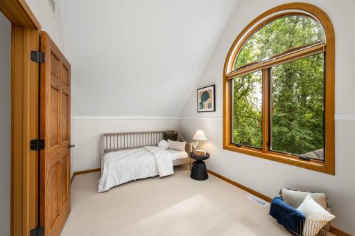 3rd Floor bedroom #3 dressed in a striking arched window window with warm wood trim frames tranquil treetop views