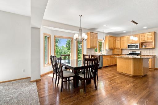Open kitchen and dining with hardwood floors and wooded backyard views.