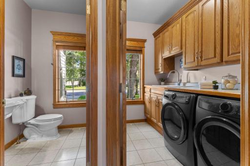 A spacious laundry room with built-in cabinets and countertop, a washer, dryer, sink, and front yard views .