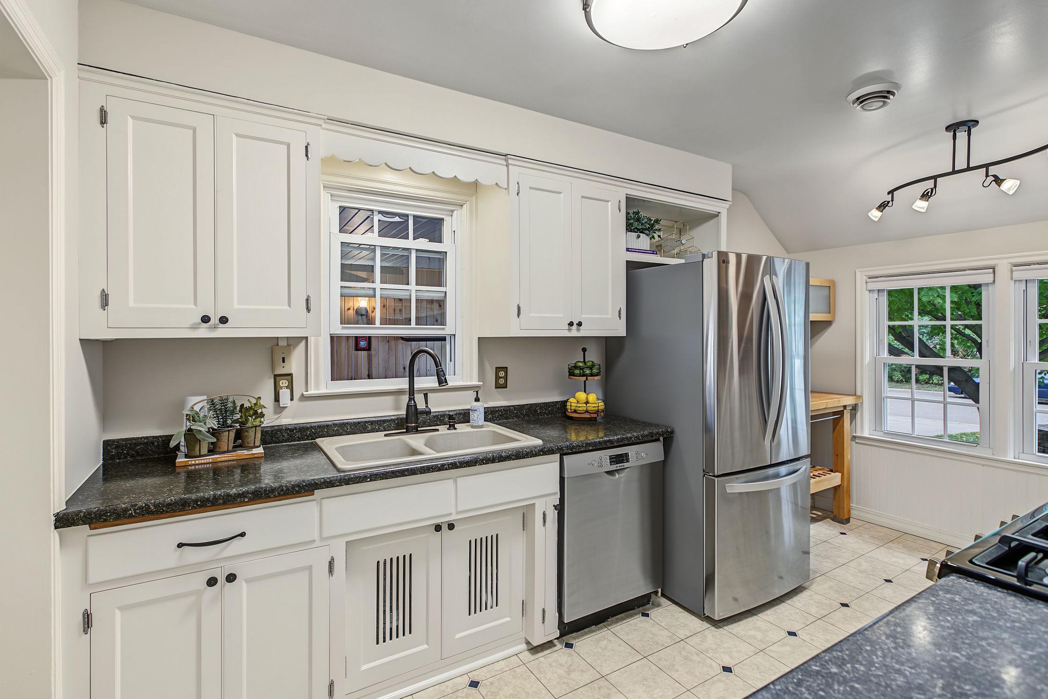 The updated vintage kitchen features modern stainless steel appliances including a gas range, freshly enameled original cabinetry and additional butcher block prep space near the windows.