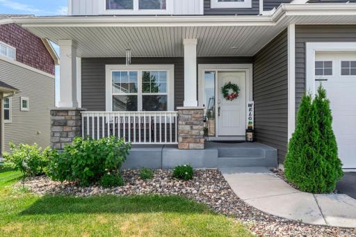 Inviting covered front porch complete with stone-wrapped pillars, low-maintenance river rock landscaping, and a welcoming front doorway.