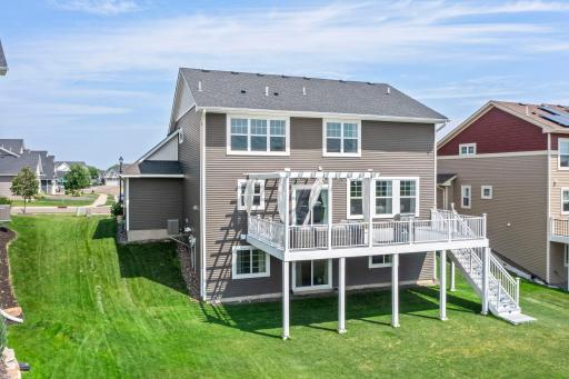 High-angle shot capturing the entire back exterior layout, full deck with stairs, side yard, and neighborhood setting.