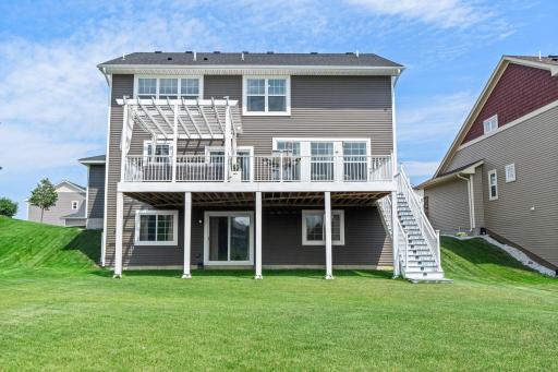 Straight-on view of the home's rear exterior, featuring the full deck staircase, covered lower patio level, and well-maintained lawn