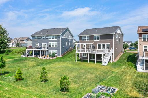 Mid-level aerial view highlighting the vast open lawn, young trees, and seamless outdoor entertainment space.