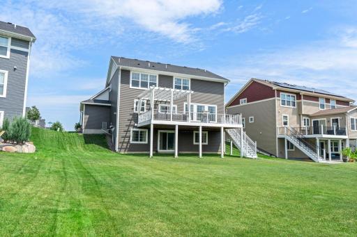 Wide perspective of the sprawling back yard lawn showcasing the home's side profile and multi-level outdoor living setup.