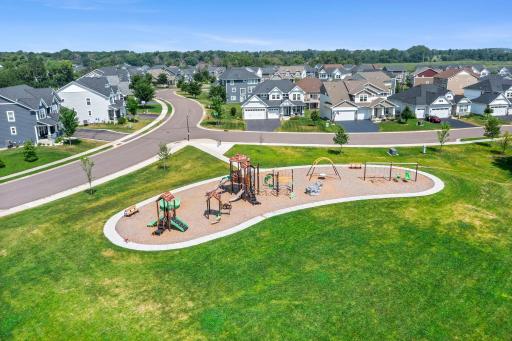 Mid-level aerial shot focusing on the community play structures, swing sets, and spacious green field.
