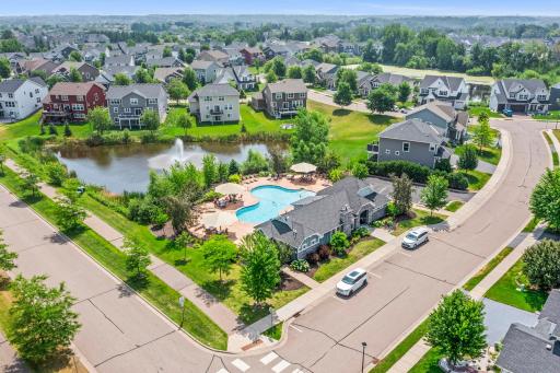Close aerial perspective of the outdoor pool, spacious patio lounging area, clubhouse, and scenic water feature.