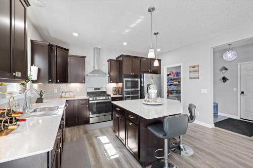 Modern kitchen equipped with dark cabinetry, quartz countertops, stainless steel gas appliances, subway tile backsplash, and a central island with seating