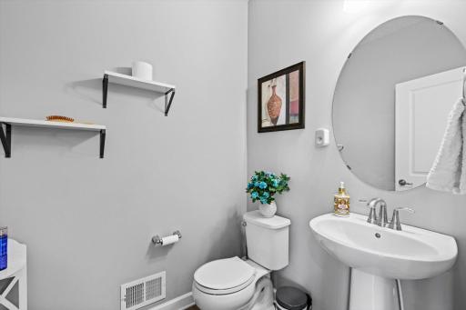 Convenient half bath featuring a stylish pedestal sink, oval mirror, and floating accent display shelves.