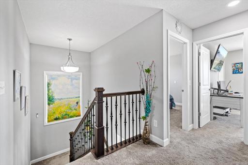Open staircase landing with dark wood railings and iron balusters, connecting the upper-level bedrooms and flex spaces.