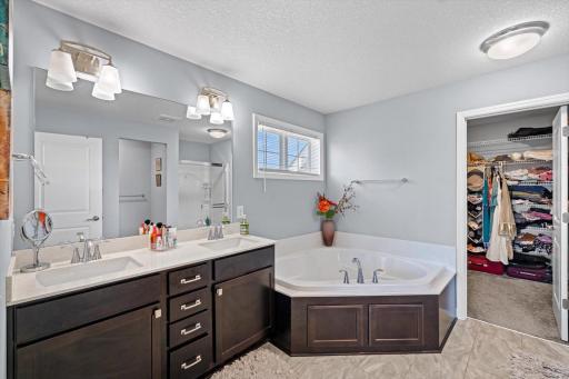 Spa-like bathroom equipped with a double sink vanity, deep corner soaking tub, tile flooring, and a walk-in closet.