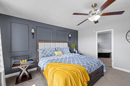 Spacious primary retreat featuring custom wall trim details, a ceiling fan, and direct access to the en-suite bath.