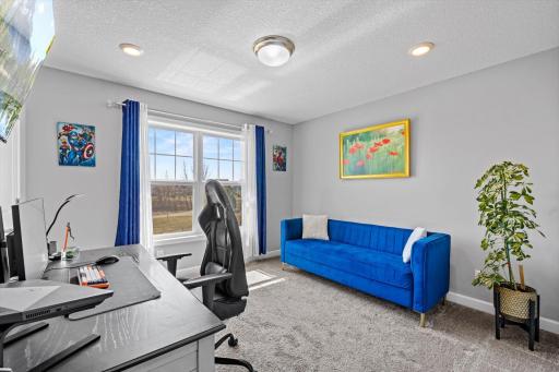 Bright secondary bedroom currently styled as a home office, featuring large windows and comfortable carpeted flooring.