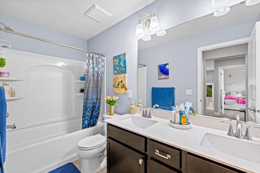 Guest bath featuring a spacious double vanity, quartz counter space, dark cabinetry, and a full shower/tub combo.